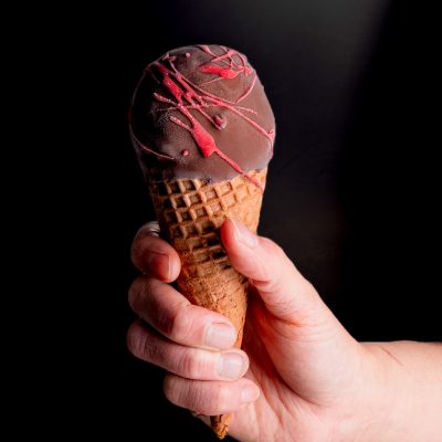 BLOOD SHOT - Waffle cone filled with cream cheese gelato, chunks of red velvet cake and red velvet topping, dipped in dark chocolate and splatters of red chocolate